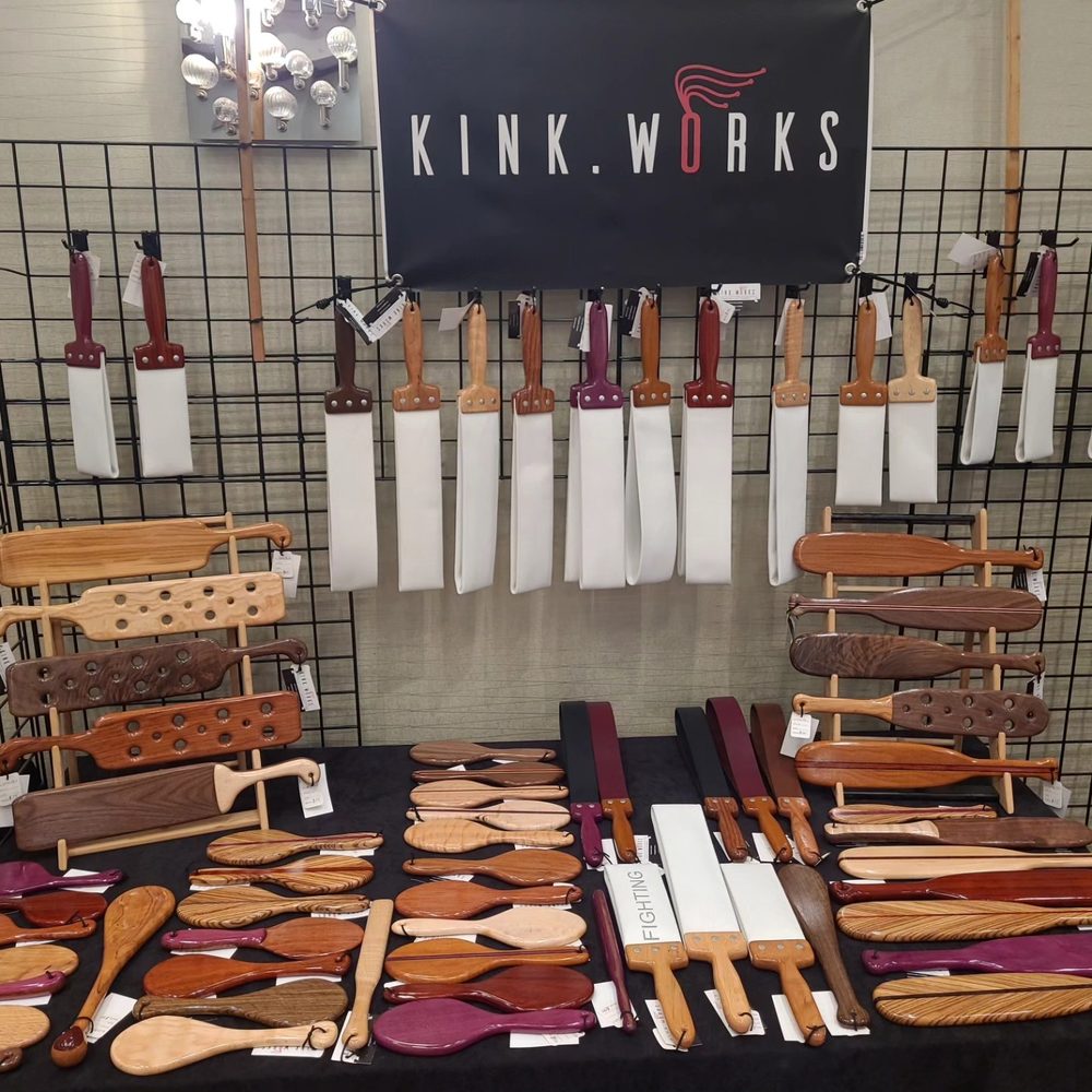 Kink.Works table with a branded banner, hanging straps and paddles laid out